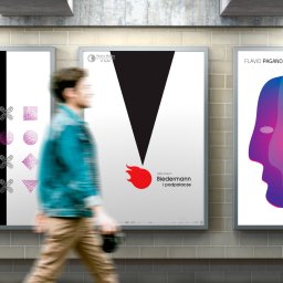 Jakub Margasiński KolorProjekt - Trzy plakaty w srebrnych ramach wiszące na ścianie z płytek, przedstawiające grafiki promujące wydarzenia kulturalne, z rozmytą sylwetką przechodzącej osoby.