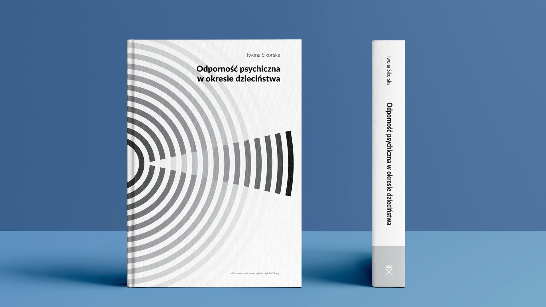 Dwa egzemplarze książki Iwony Sikorskiej 'Odporność psychiczna w okresie dzieciństwa' na niebieskim tle. Jeden egzemplarz leży płasko, ukazując okładkę z koncentrycznym wzorem, drugi stoi pionowo...