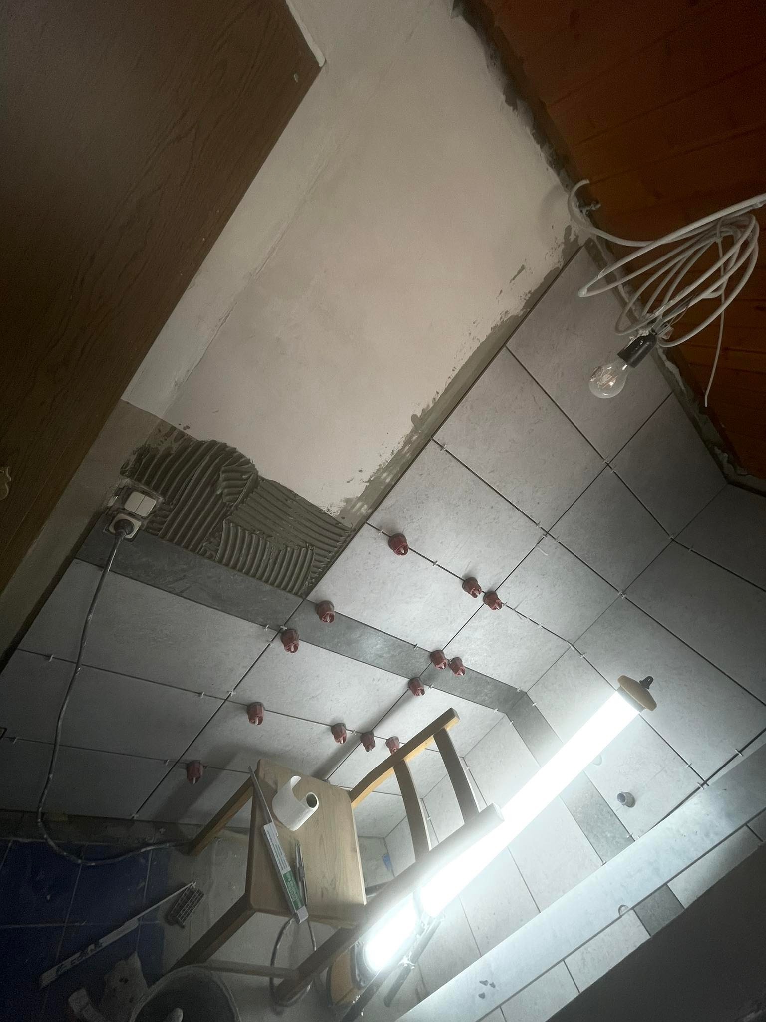 Montaż płytek na ścianie w trakcie prac wykończeniowych, widoczne poziomice i system poziomowania płytek z czerwonymi klipsami, surowy stan pomieszczenia.