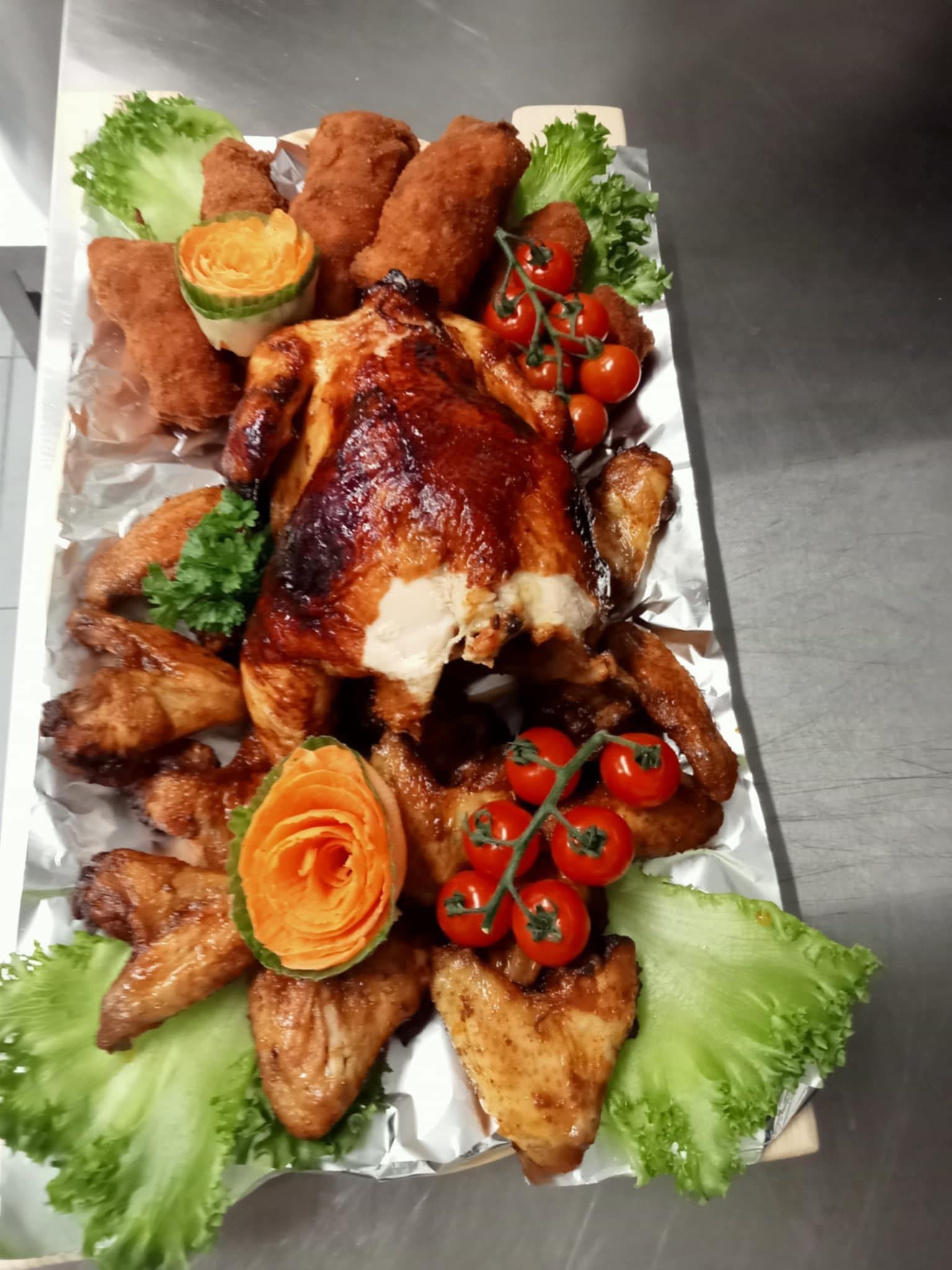 Udekorowany półmisek z pieczonym kurczakiem, smażonymi kąskami, skrzydełkami, pomidorkami cherry i sałatą, z ozdobnymi rzeźbami z warzyw.