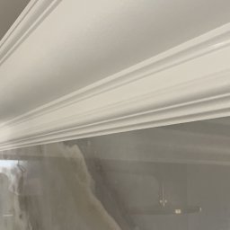 PZ PROJECT - Biała listwa dekoracyjna zamontowana na styku ściany z sufitem, widoczne detale profilu i wykończenie ściany imitujące marmur.