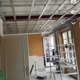 PZ PROJECT - Montaż metalowej konstrukcji podwieszanego sufitu w trakcie remontu mieszkania, widoczne profile, drabina i fragmenty instalacji.