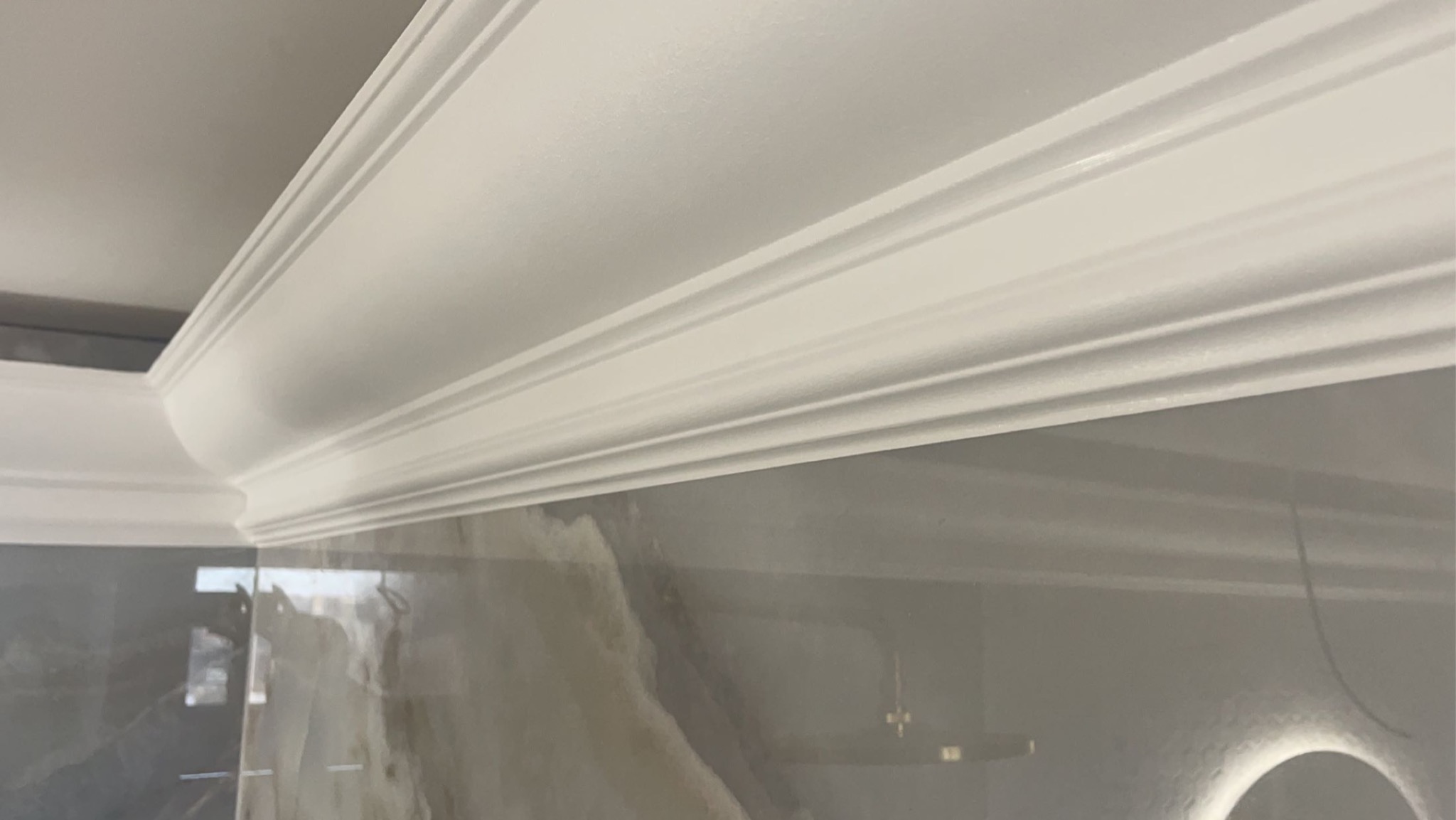 Biała listwa dekoracyjna zamontowana na styku ściany z sufitem, widoczne detale profilu i wykończenie ściany imitujące marmur.