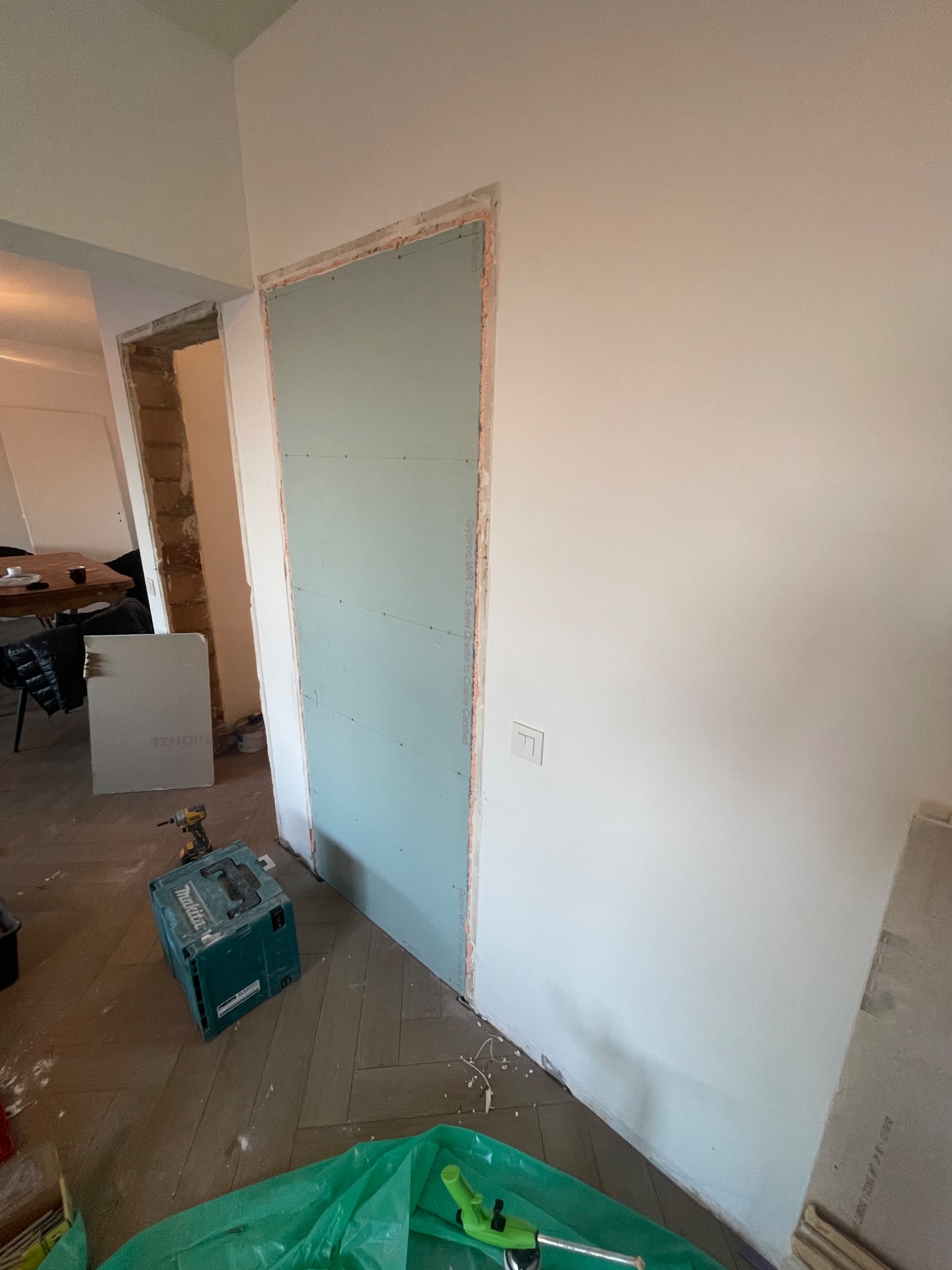 Ściana z zamontowaną zieloną płytą karton-gips przed szpachlowaniem, widoczne narzędzia, podłoga parkiet w jodełkę.