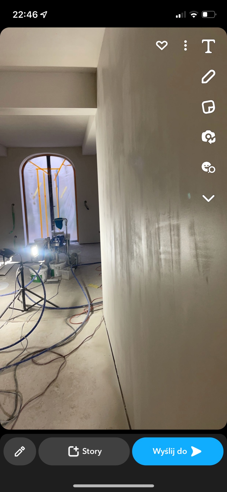 Świeżo położona, jasna gładź na ścianie w trakcie schnięcia, widoczny sprzęt do natrysku gładzi, zabezpieczone okno łukowe folią malarską.