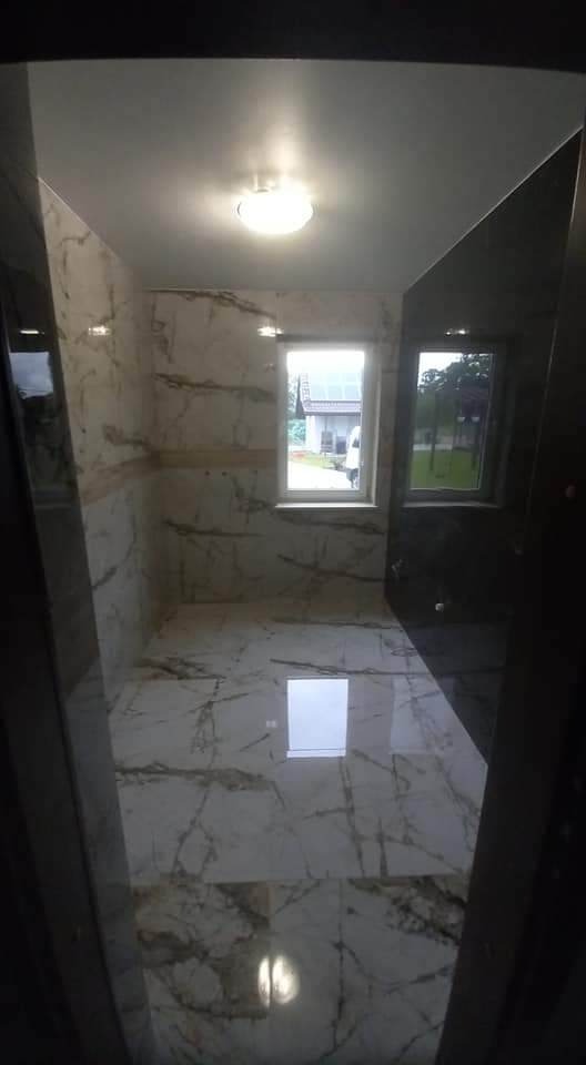 Wykończona łazienka z marmurowymi płytkami na ścianach i podłodze, widok z progu, okno z widokiem na dom z fotowoltaiką.