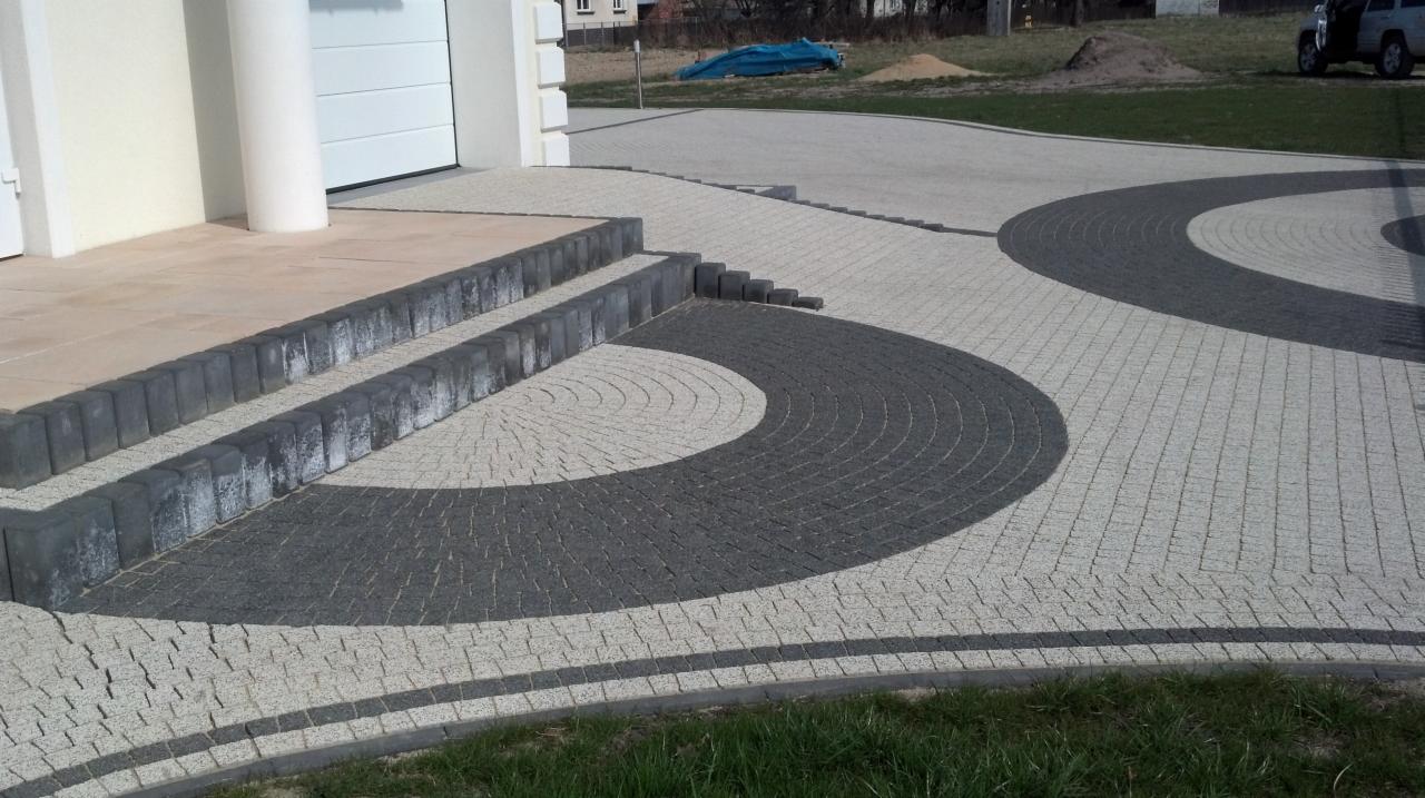 Ułożona kostka brukowa w dwóch odcieniach szarości tworząca wzór półkola i łuków przed wejściem do domu z białymi kolumnami.