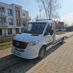 My dreams Justyna Kowalewska - Biała autolaweta Mercedes na chodniku, z napisem 'Pomoc Drogowa' na boku, zaparkowana przed nowoczesnym budynkiem mieszkalnym w słoneczny dzień.