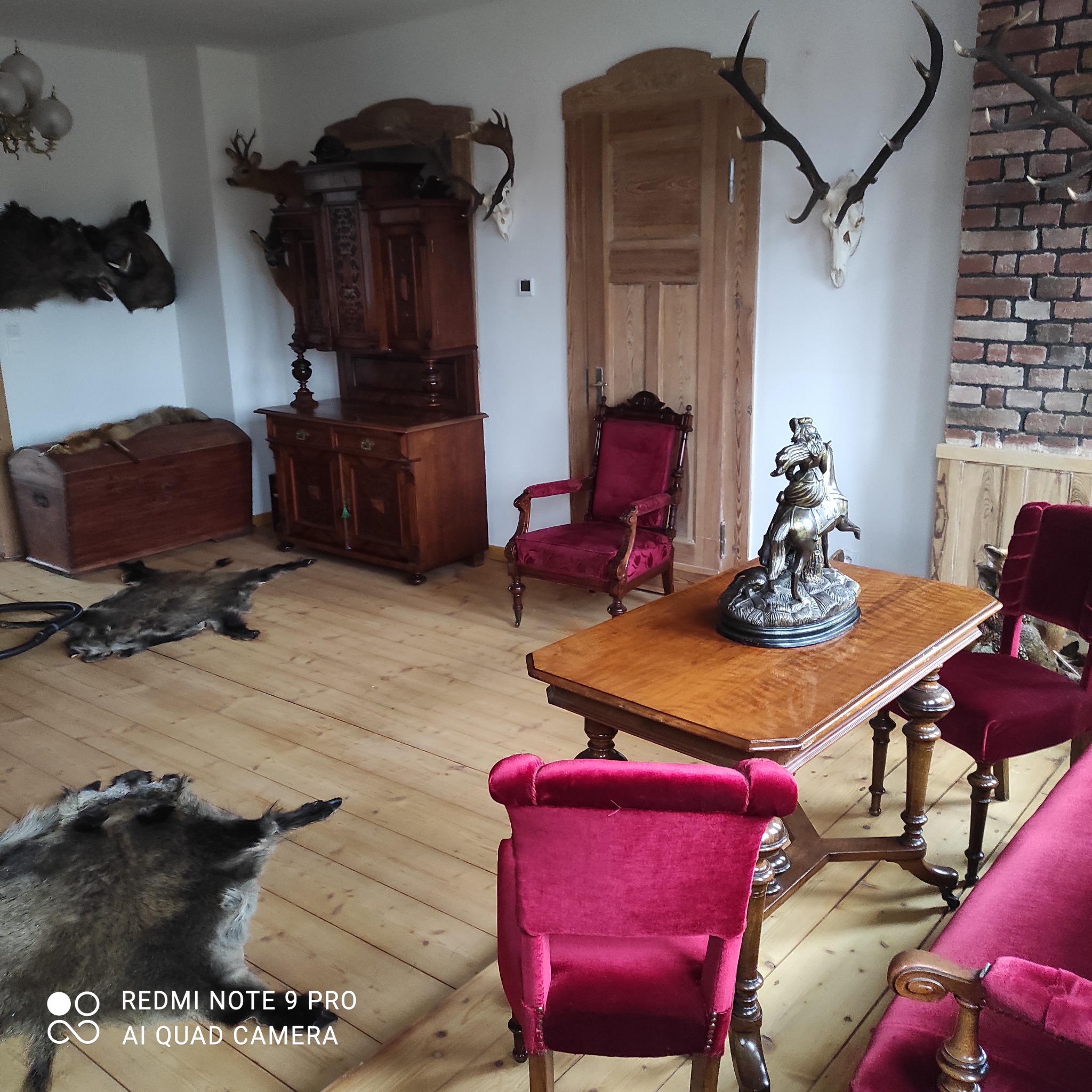 Salon w stylu myśliwskim z trofeami, skórami zwierząt, antycznymi meblami i rzeźbą jeźdźca na komodzie