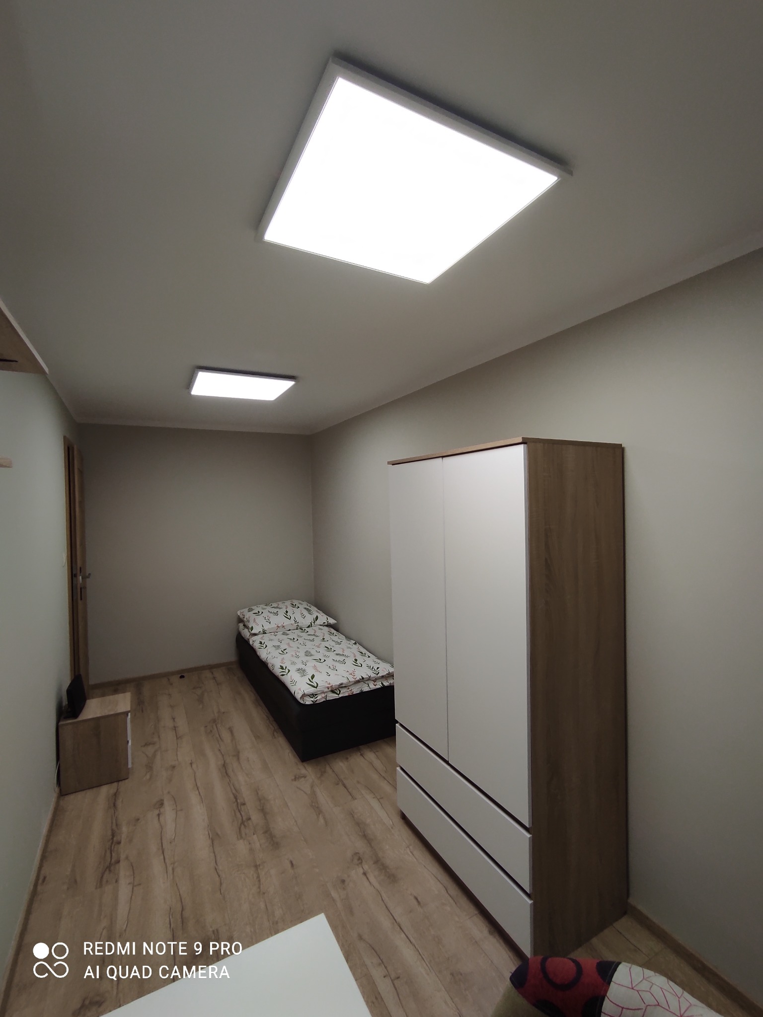 Pokój z łóżkiem, szafą i dwoma kwadratowymi lampami sufitowymi, widok z dołu.