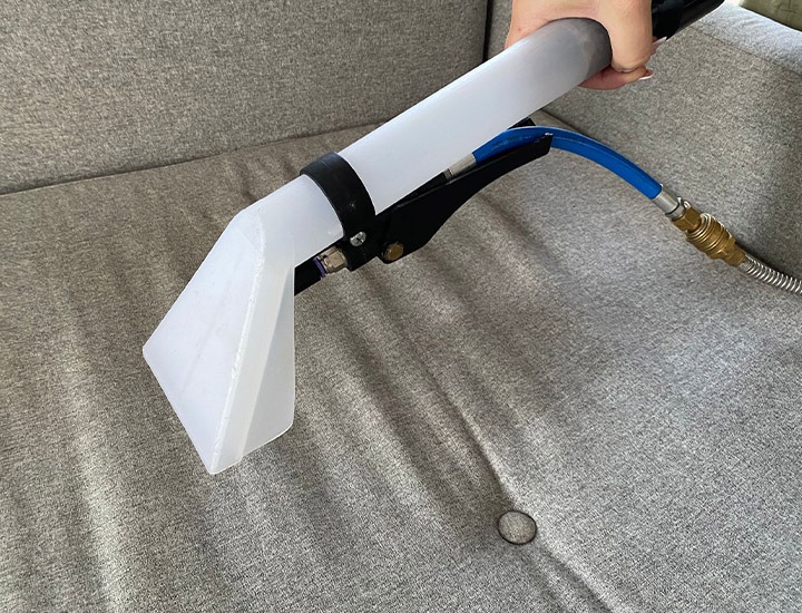 Dysza urządzenia ekstrakcyjnego do czyszczenia tapicerki, zbliżenie na szarą kanapę podczas pracy.