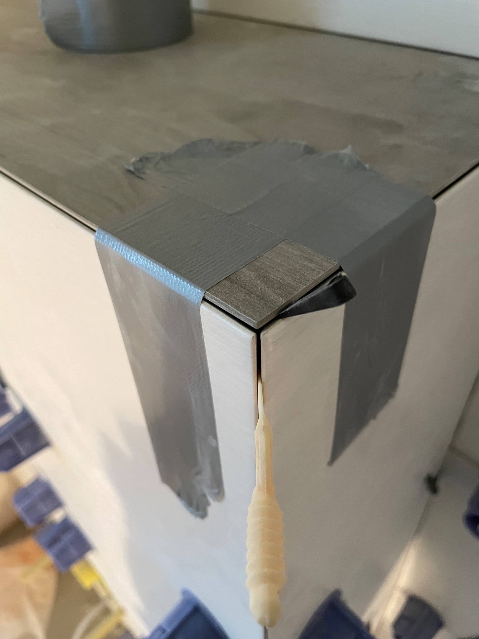 Detail of corner tiling with gray duct tape securing the edges, plastic spacers visible, showcasing a work-in-progress tiling job.