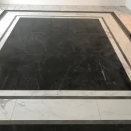 Podłoga wyłożona czarno-białymi płytkami z marmurkowym wzorem, ułożonymi w kwadratową ramę z ciemniejszymi płytkami w centrum.