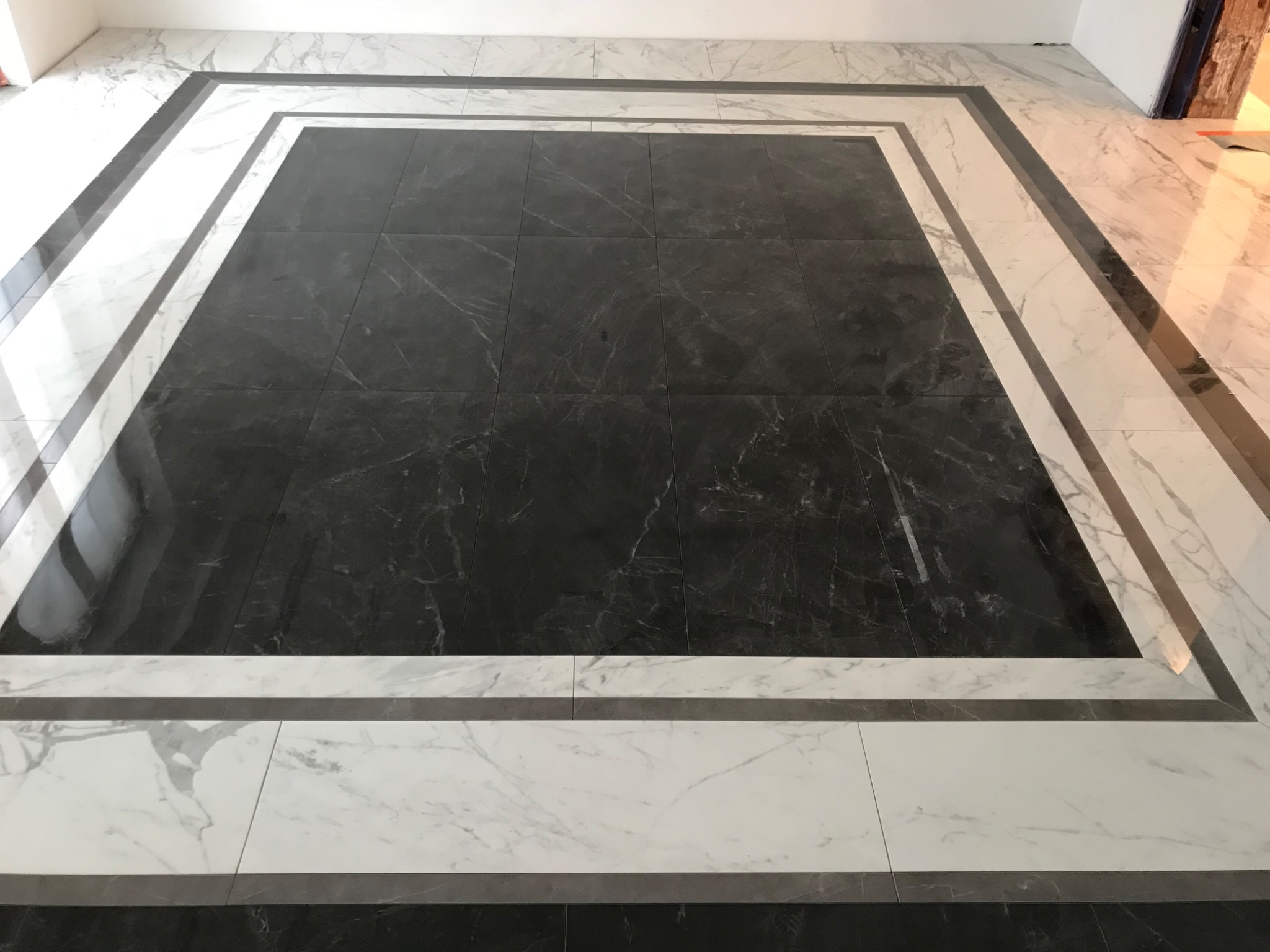 Podłoga wyłożona czarno-białymi płytkami z marmurkowym wzorem, ułożonymi w kwadratową ramę z ciemniejszymi płytkami w centrum.