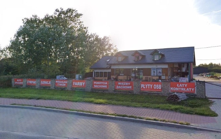 Fasada budynku z reklamami materiałów budowlanych: płyty G-K, styropian, elewacje, mieszalnia tynków, farby, pokrycia dachowe, więźby dachowe, płyty OSB, łaty kontrałaty. Widok z chodnika.