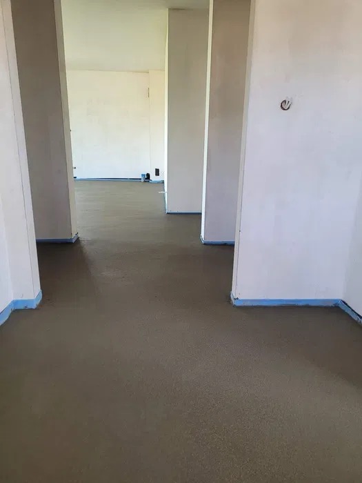 Świeżo wylana, gładka posadzka w pomieszczeniu z kolumnami, zabezpieczona niebieską taśmą przy ścianach.