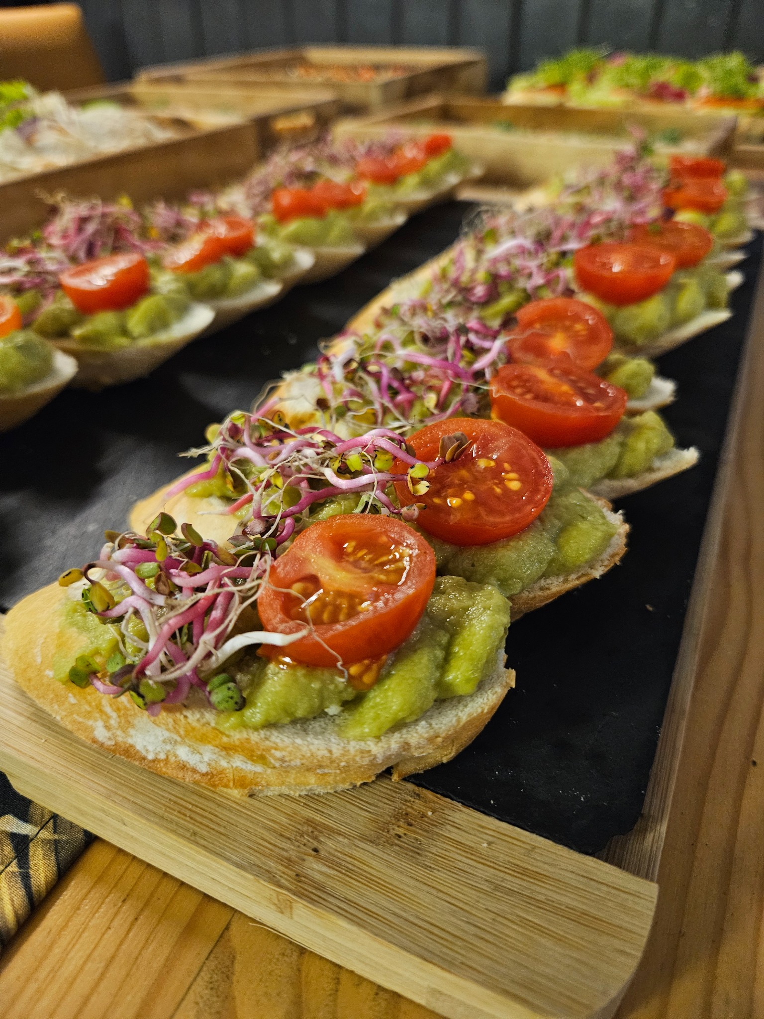 Baguette z pastą z awokado, pomidorem i kiełkami na czarnej desce. Eleganckie przekąski cateringowe, zbliżenie na detale, naturalne światło.