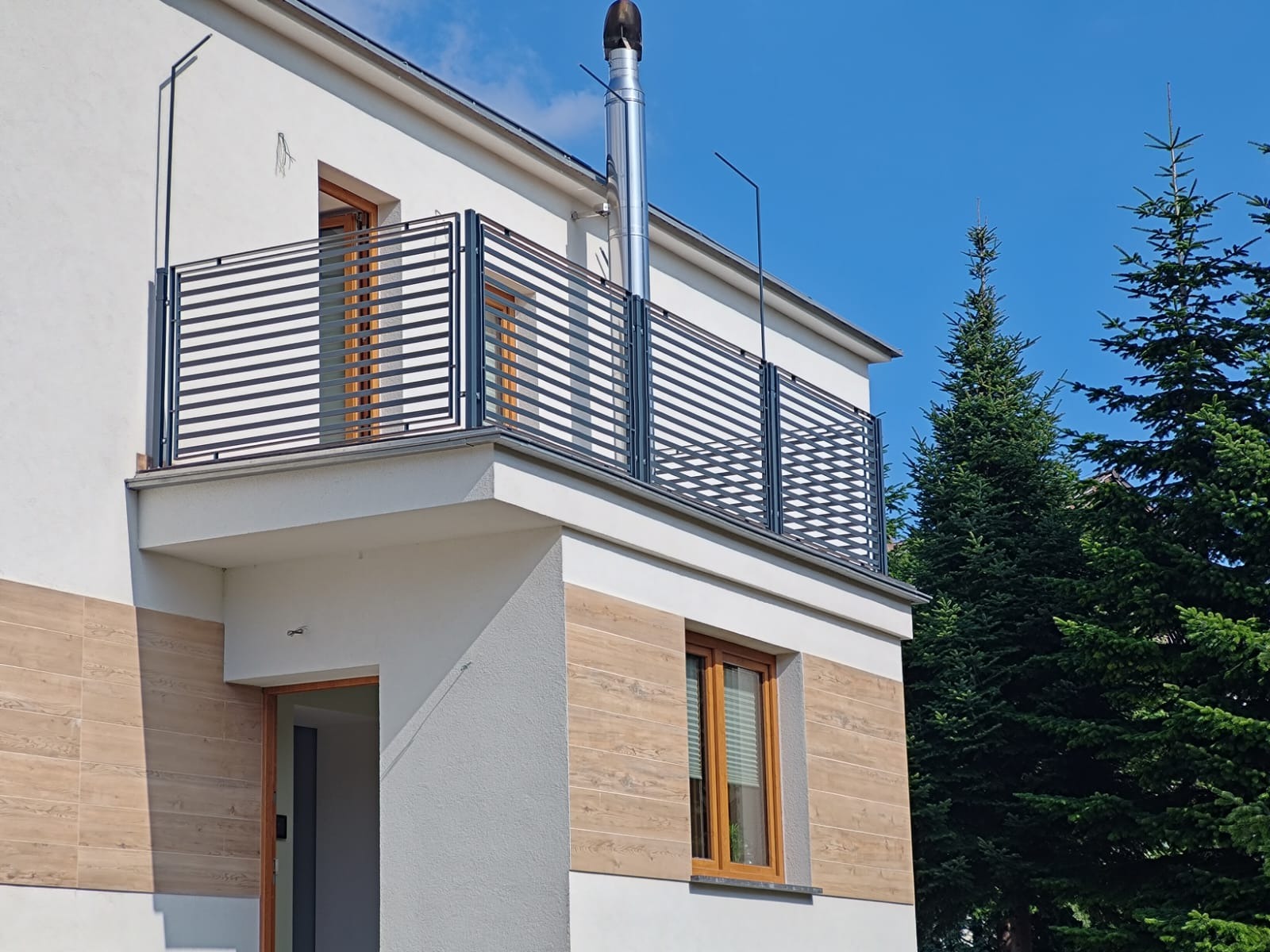 Nowoczesna balustrada balkonowa z poziomych profili metalowych, zamontowana w nowym domu z jasną elewacją i elementami dekoracyjnymi imitującymi drewno.