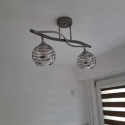 Dwupunktowa lampa sufitowa z dekoracyjnymi, szklanymi kloszami w kształcie kuli, zamontowana na białym suficie w nowoczesnym wnętrzu. Widoczne okno z żaluzjami.