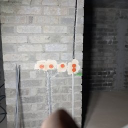 EL-ROB - Surowa ściana z cegły z puszkami elektrycznymi i przewodami w Kawęczynie. Widoczne kable i otwory pod gniazdka przed tynkowaniem. Instalacja w trakcie prac.