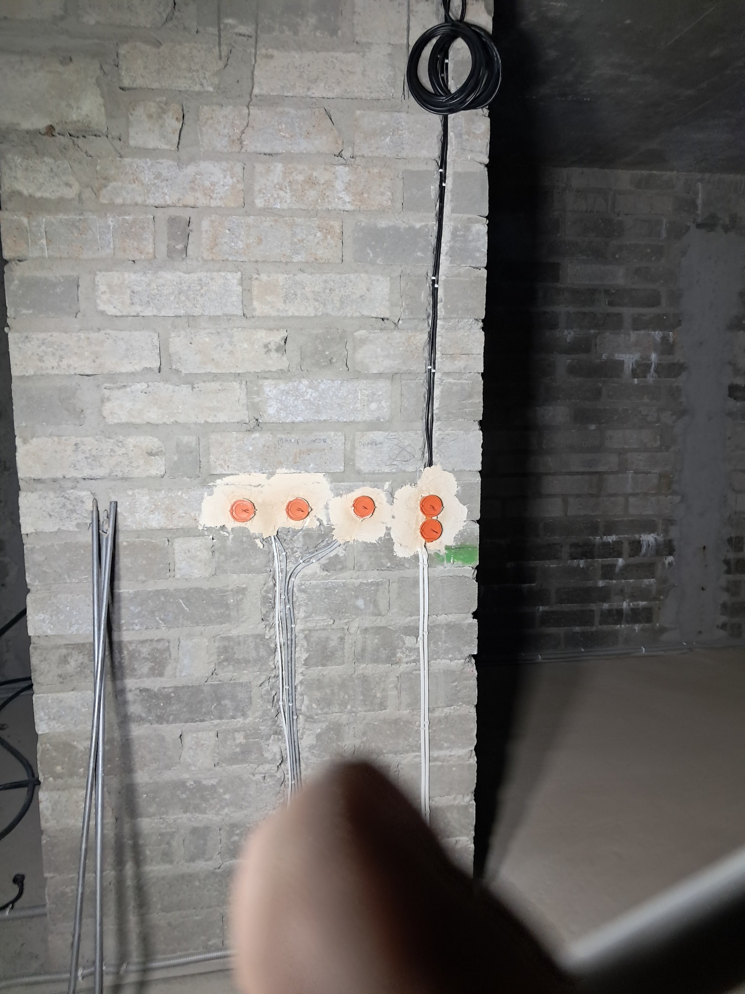 Surowa ściana z cegły z puszkami elektrycznymi i przewodami w Kawęczynie. Widoczne kable i otwory pod gniazdka przed tynkowaniem. Instalacja w trakcie prac.