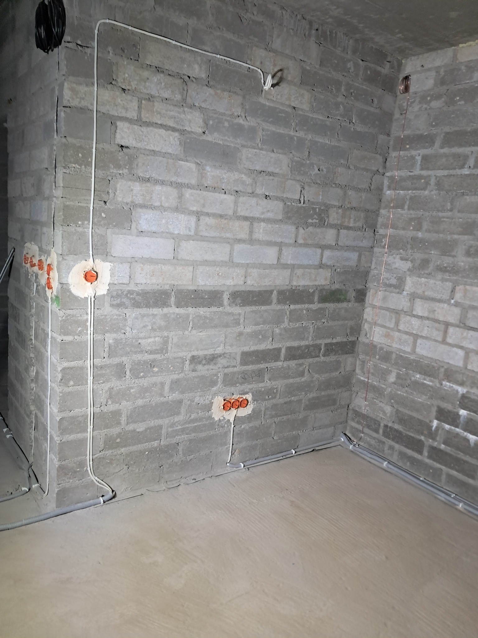 Surowy mur z instalacją elektryczną: kable w peszlu, puszki podtynkowe. Etap prac przed tynkowaniem.