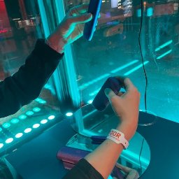 Kamil Milewski usługi Remontowo-Budowlane - Dwie osoby trzymają w dłoniach niebieskie przedmioty na tle neonowego oświetlenia i odbić w lustrach. Widoczny fragment nadgarstka z opaską.