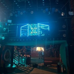 Kamil Milewski usługi Remontowo-Budowlane - Oświetlona konstrukcja sceniczna z neonowym logo 'X' i reflektorami, widoczna z dołu, z elementami schodów i sylwetkami osób w tle.