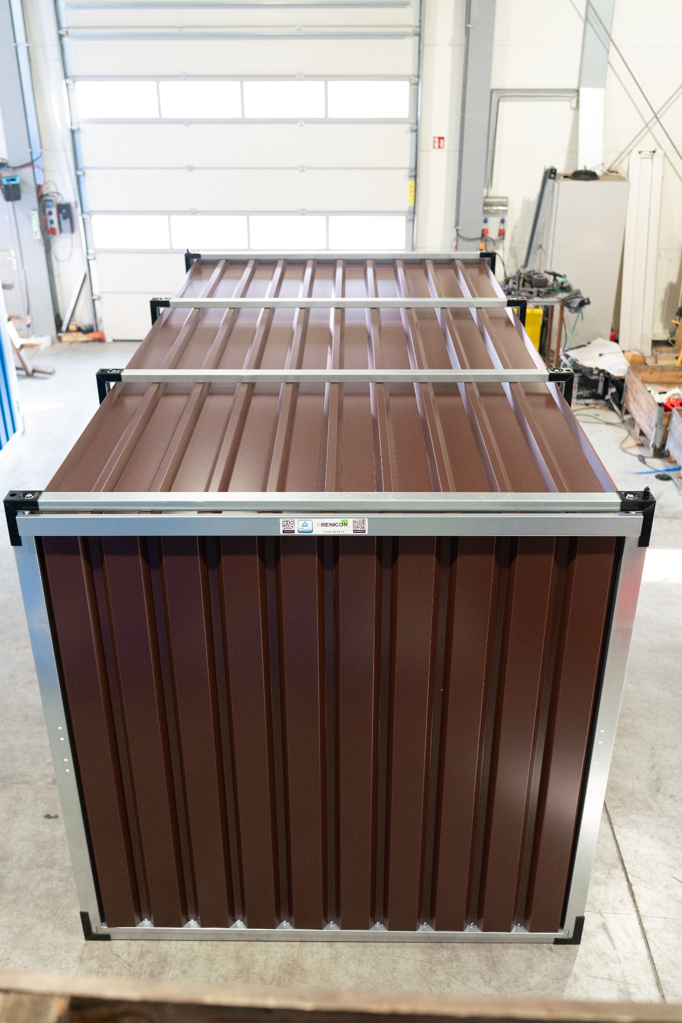 Brązowy kontener magazynowy z metalowymi wzmocnieniami, widok z góry na tle hali z bramą.