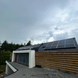 Nowoczesny dom z panelami słonecznymi na dachu i drewnianą elewacją, widok z dołu w pochmurny dzień.