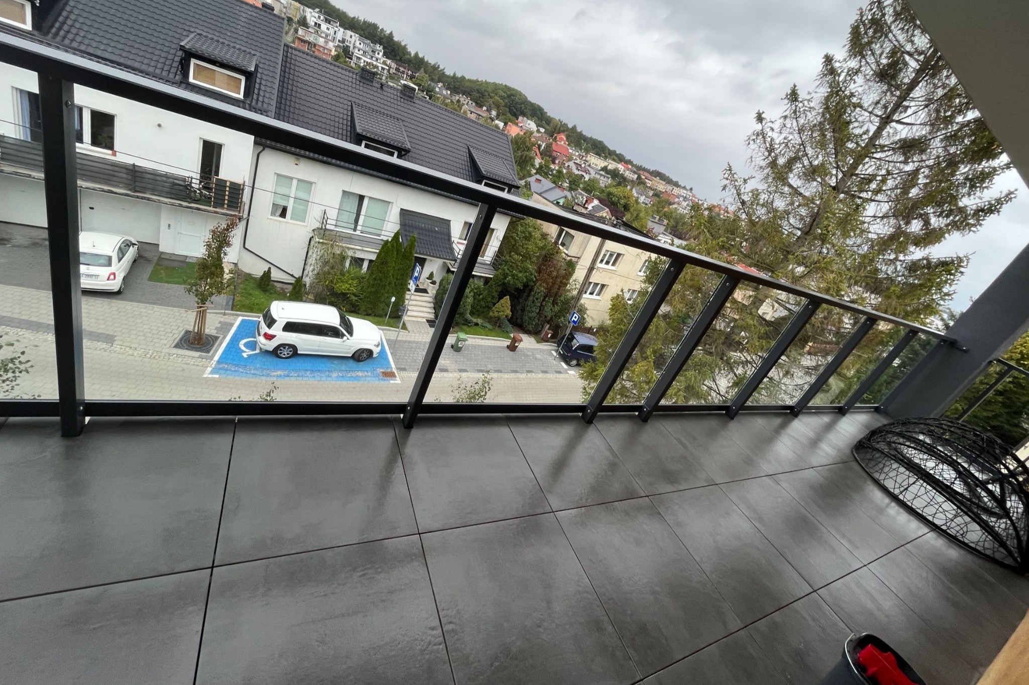 Widok z balkonu na osiedle domów jednorodzinnych w pochmurny dzień, szare płytki na podłodze, przeszklona balustrada.