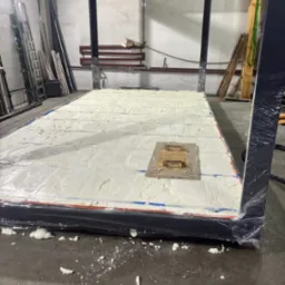 Konstrukcja z pianką PUR, widoczne zabezpieczenia folią. Detal ocieplenia, z elementami drewnianymi na powierzchni. W tle drabiny i narzędzia.