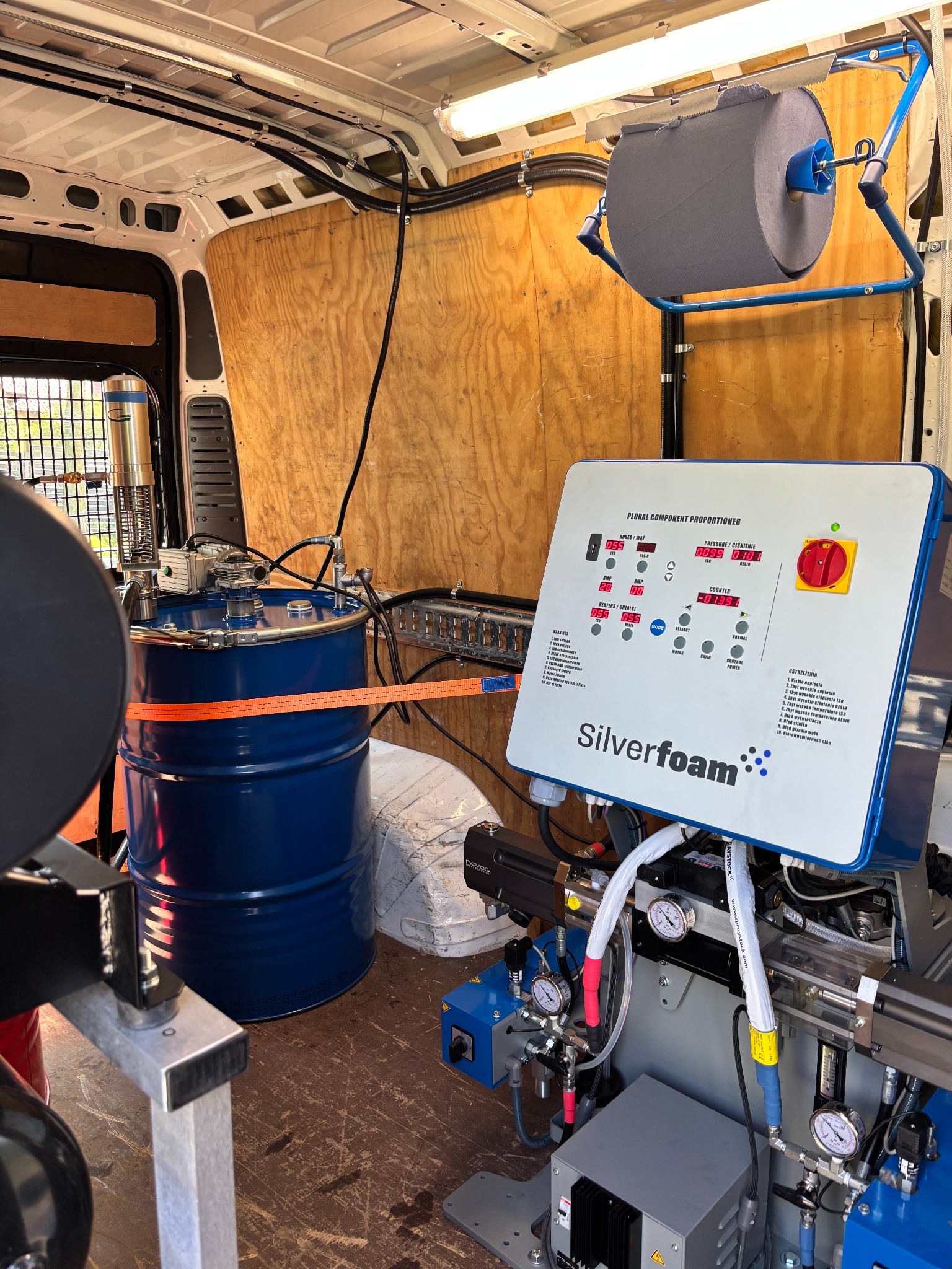 Wnętrze furgonetki z maszyną Silverfoam do ocieplania pianką PUR, widoczny niebieski beczka z komponentami i panel sterowania z wyświetlaczami.