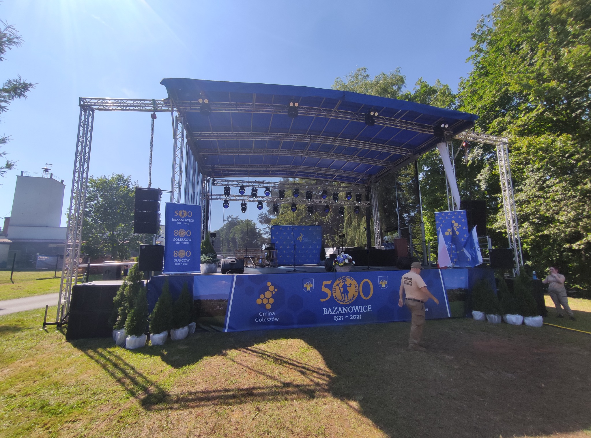 Scena plenerowa z konstrukcją aluminiową, nagłośnieniem i oświetleniem, przygotowana na imprezę plenerową Gminy Goleszów i Bażanowice, widoczne banery reklamowe i dekoracyjne drzewka.