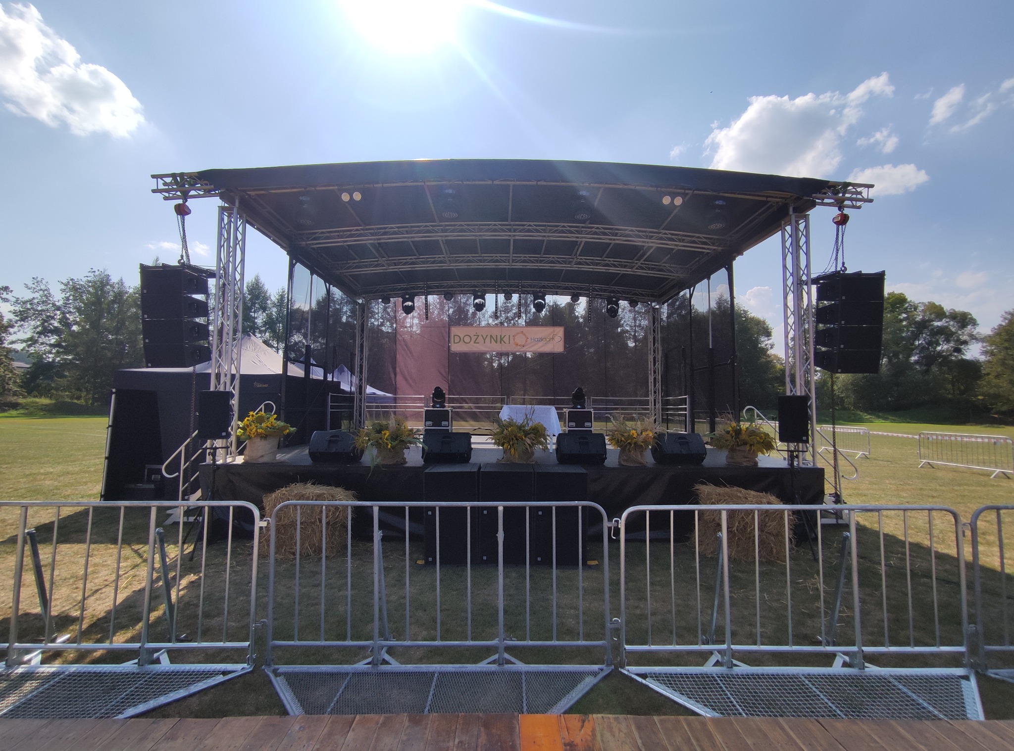 Scena plenerowa z nagłośnieniem i oświetleniem przygotowana na dożynki, dekoracje z siana i kwiatów, barierki zabezpieczające.