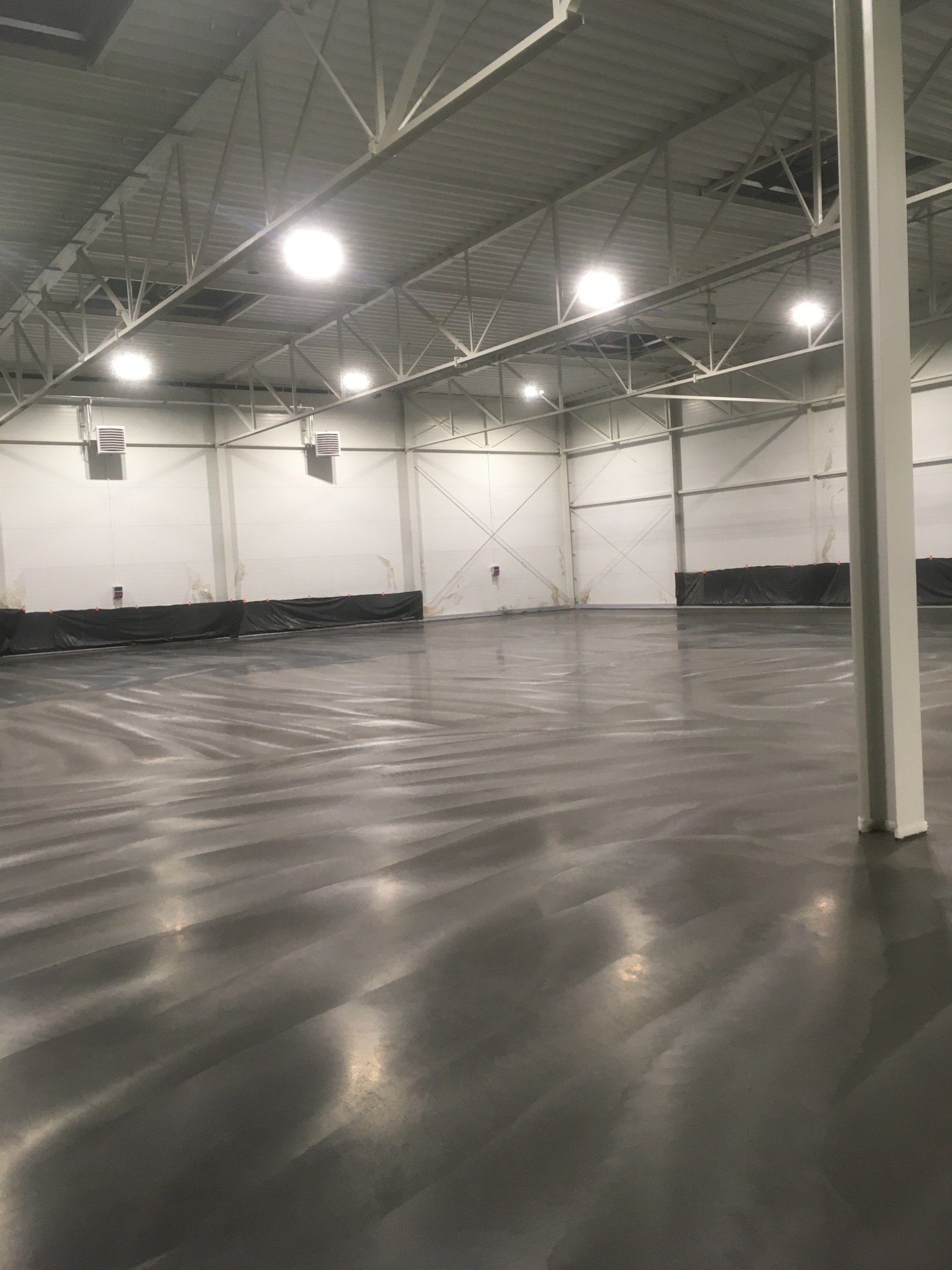 Świeżo wylana, błyszcząca posadzka przemysłowa w hali magazynowej, widoczne zabezpieczenia ścian folią.
