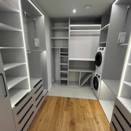 Brzostowski Meble - Jasnoszara garderoba na wymiar z oświetleniem LED, drewnianą podłogą i pralką w zabudowie.