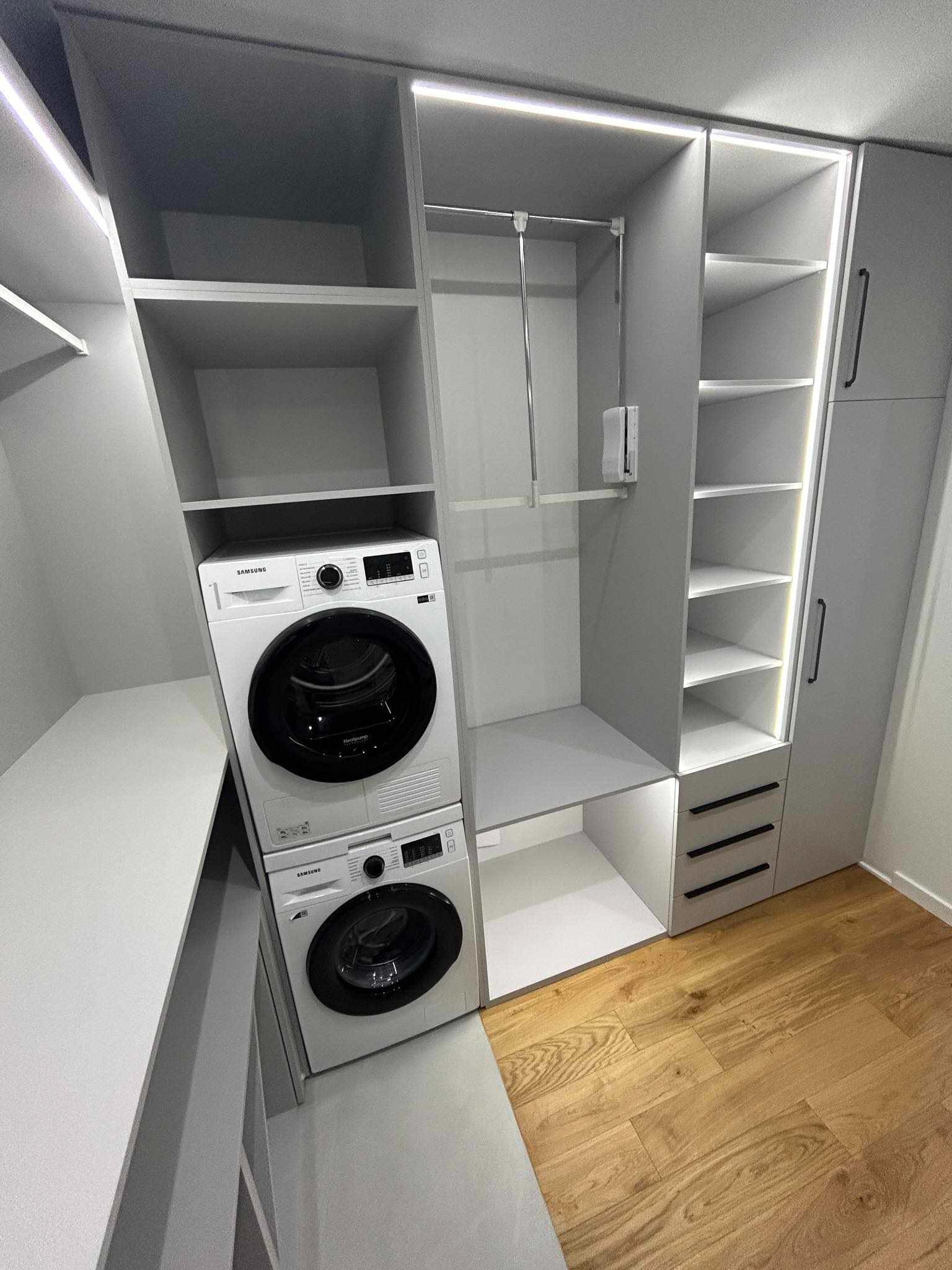 Szara szafa na wymiar z wbudowaną pralką i suszarką Samsung, podświetlane półki, drewniana podłoga.