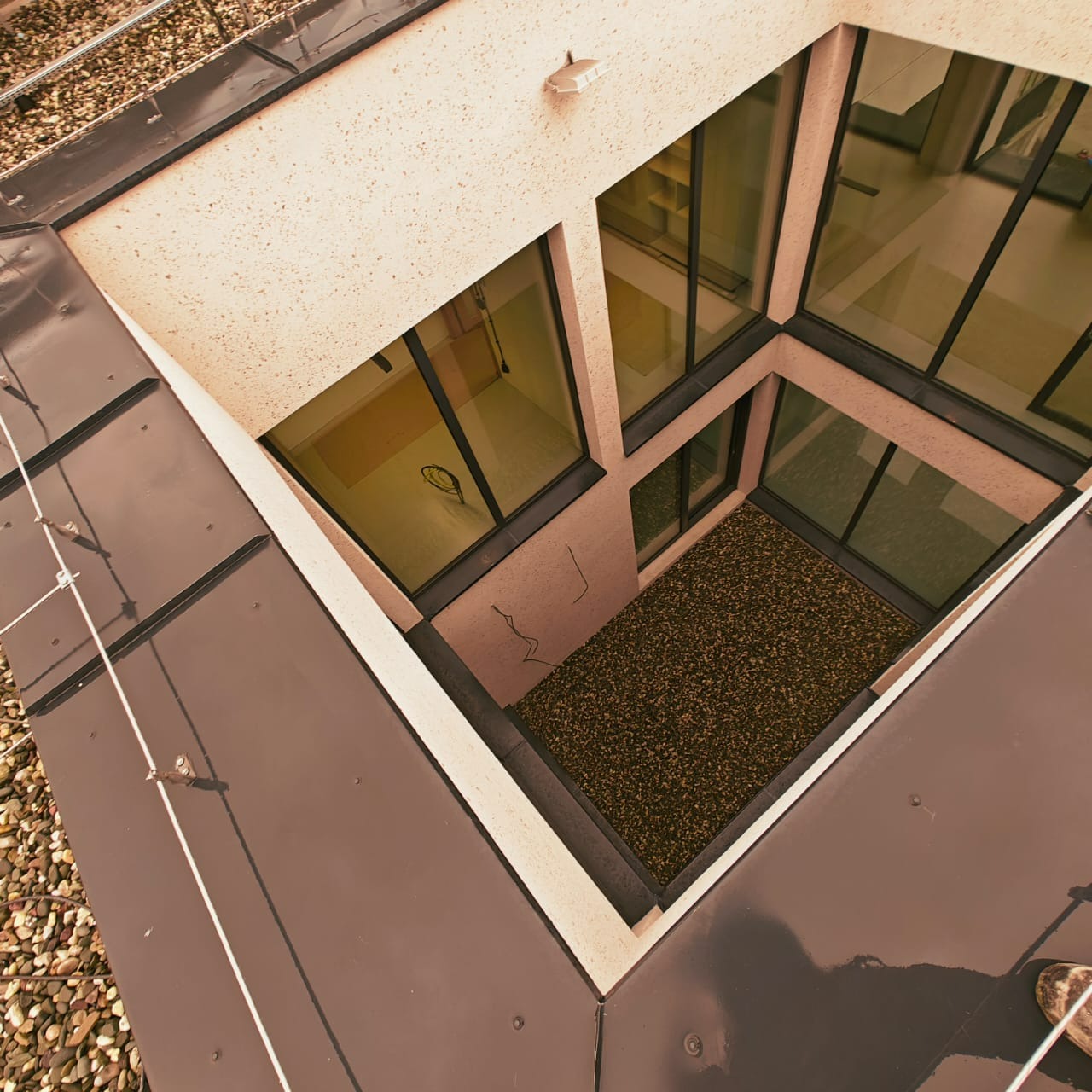 Nowoczesna elewacja budynku z oknami, widok z góry na wewnętrzny dziedziniec z kamieniami. Dach pokryty blachą z widocznymi elementami mocującymi.