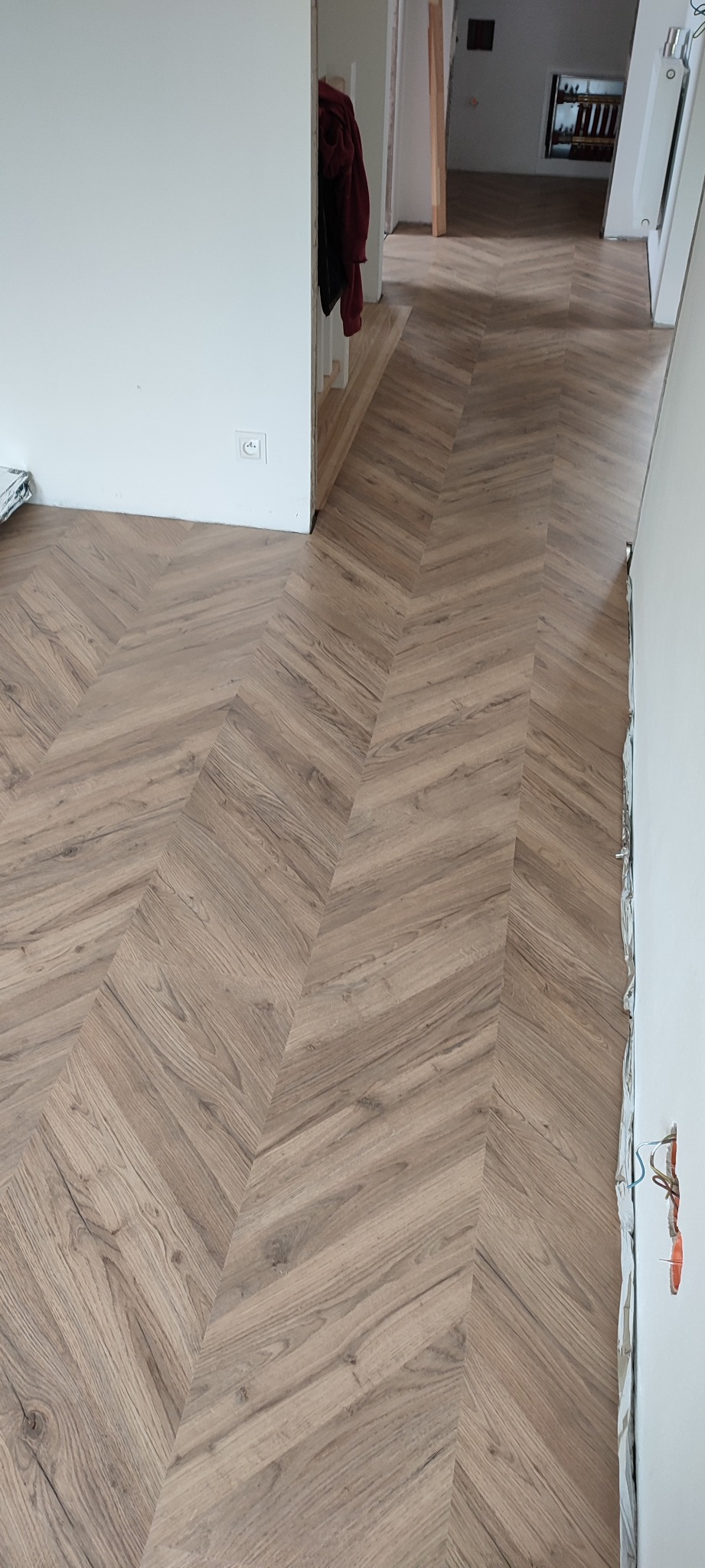 Ułożone panele podłogowe w jodełkę, widoczne kable wystające ze ściany i fragment garderoby w tle.