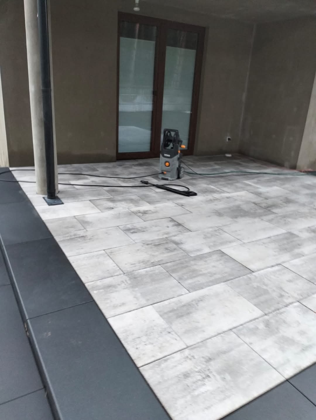 Świeżo ułożona, jasnoszara kostka brukowa na tarasie w Radomsku, z widoczną myjką ciśnieniową przygotowaną do czyszczenia, obok ciemnoszary obrzeże.