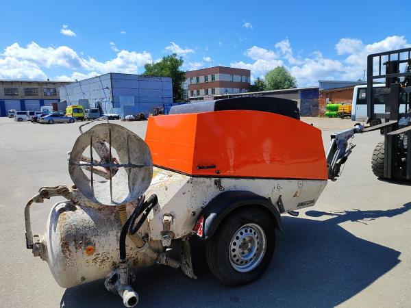 Agregat tynkarski z pomarańczową obudową i mieszadłem, zaparkowany na placu budowy, widoczny wózek widłowy w tle.