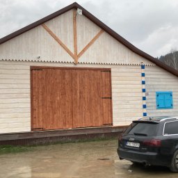 Fox House - Nowo wybudowany drewniany budynek gospodarczy z dwuspadowym dachem, ozdobnymi detalami i dużymi drewnianymi drzwiami garażowymi, zaparkowany obok samochód osobowy Audi.