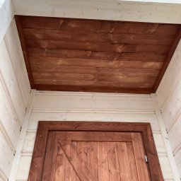 Fox House - Drewniana konstrukcja altany z brązowym, lakierowanym sufitem i drzwiami typu stodoła, widoczne elementy z jasnego, surowego drewna.