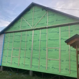 Budynek w trakcie ocieplania, widoczna zielona membrana Eurovent i drewniane listwy pionowe, fragment ściany obłożony sidingiem.