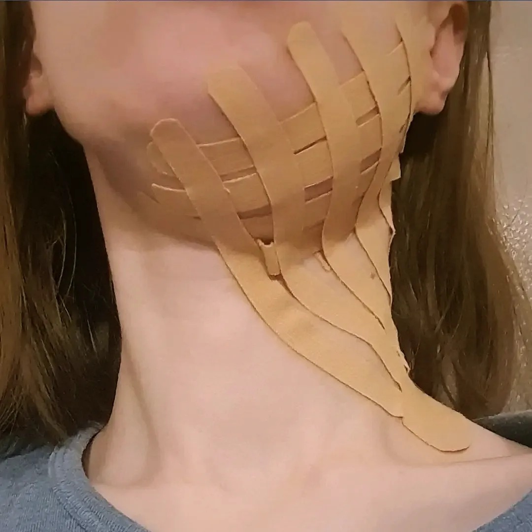 Kobieta z aplikacją kinesiotapingu na szyi i żuchwie, widok z bliska, neutralne tło.