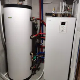 Biały zbiornik akumulacyjny i pompa ciepła Nibe z podłączonymi rurami w kotłowni w Wargowie, widoczne płytki ceramiczne na ścianach i podłodze.