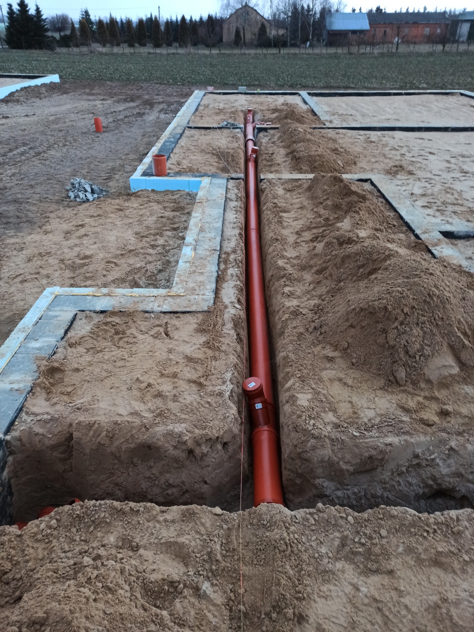 Wykonana instalacja kanalizacyjna z rur PCV w wykopie fundamentowym, widoczne szalunki i grunt.
