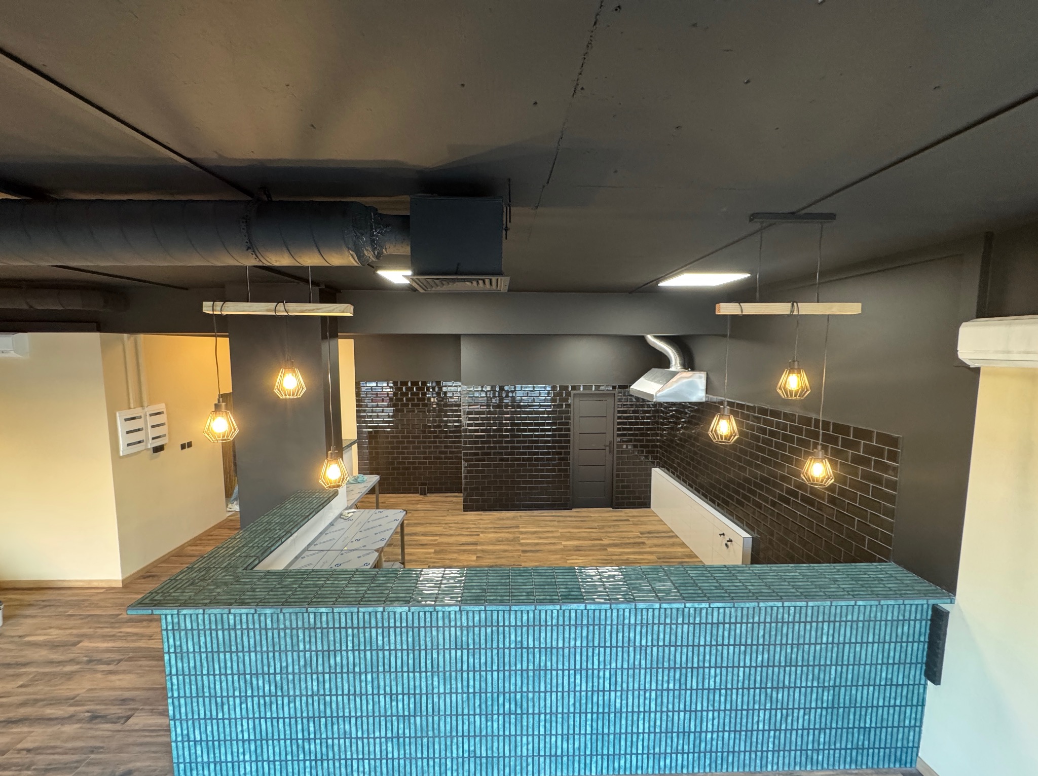 Wykończone wnętrze biurowe w Warszawie z turkusową ladą recepcyjną z płytek, czarną ścianą z płytek i nowoczesnym oświetleniem.