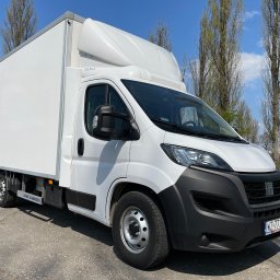 DOSTAWCZE24 SPÓŁKA Z OGRANICZONĄ ODPOWIEDZIALNOŚCIĄ SPÓŁKA KOMANDYTOWA - Biały samochód dostawczy Fiat Ducato z zabudową kontenerową, zaparkowany na betonowym placu w słoneczny dzień.